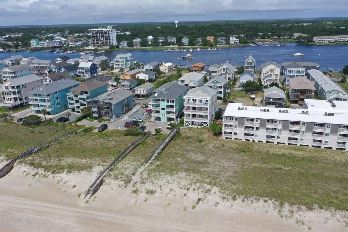 A lively waterfront scene showcasing the sandy beach, ocean, neighboring waterfront properties, and a boardwalk. Boats are visible, and the mood is inviting, suggesting both relaxation and the vibrancy of the coastal lifestyle.