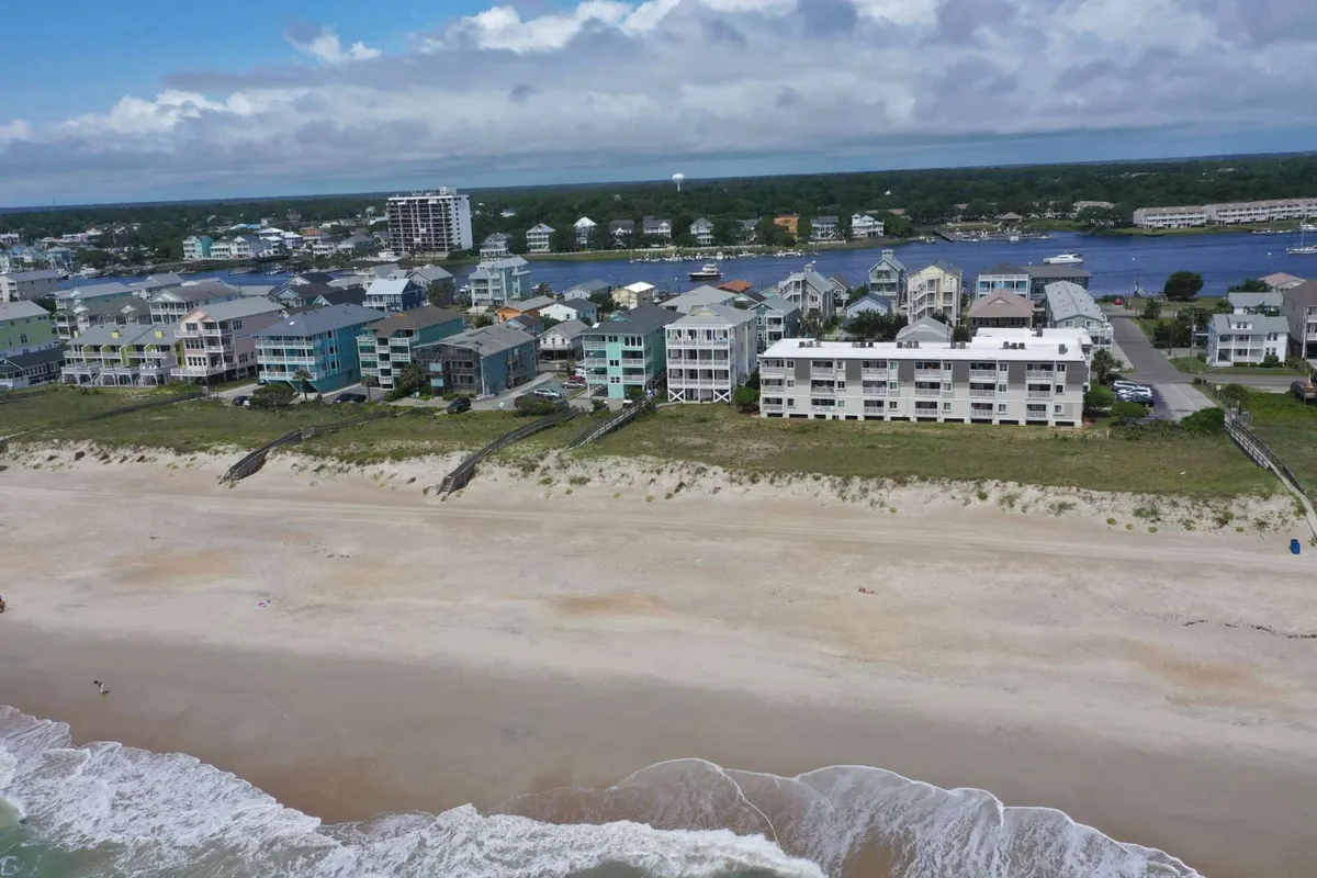 A tranquil beachfront scene featuring colorful houses lining the shore, gentle ocean waves, and a wide sandy expanse. The setting feels welcoming, perfect for families, friends, and pets enjoying the outdoors together.