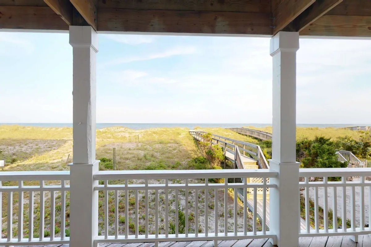 A serene oceanfront view with a sandy beach, natural dunes, and a private wooden boardwalk leading directly to the shore. The image evokes the feeling of easy, direct access from the property to the beach.