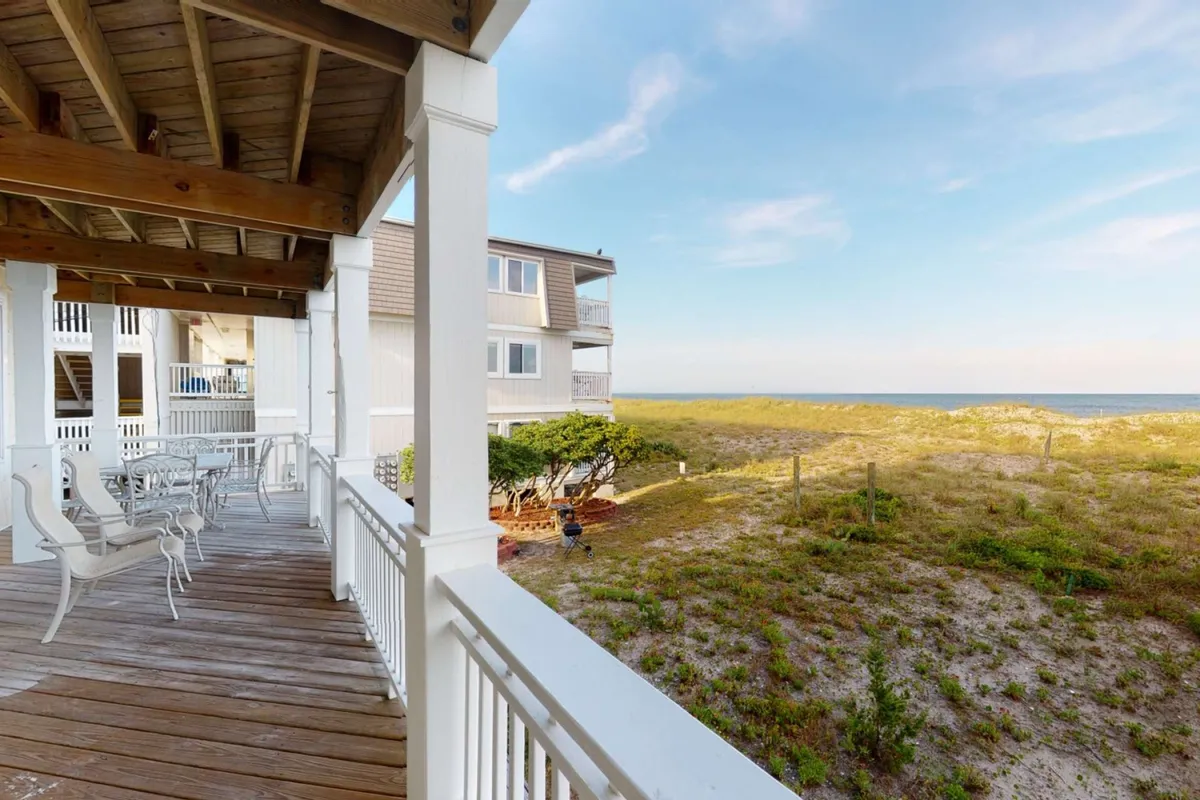An inviting wooden deck overlooks a sweeping ocean view, with outdoor dining furniture and lush vegetation nearby. The deck is positioned to catch the sunrise or sunset, making it ideal for al fresco meals, sunbathing, or coffee while soaking in the sounds of the waves.