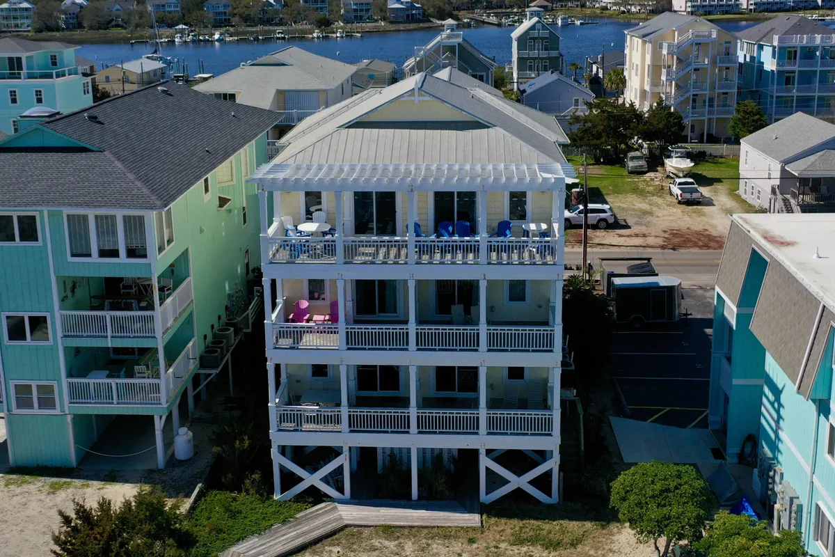 This photo features the three-story house with multiple balconies furnished with chairs, overlooking a tranquil waterway, and surrounded by neighboring homes. The image suggests relaxation, conversation, and appreciation of the peaceful water views from private outdoor spaces.