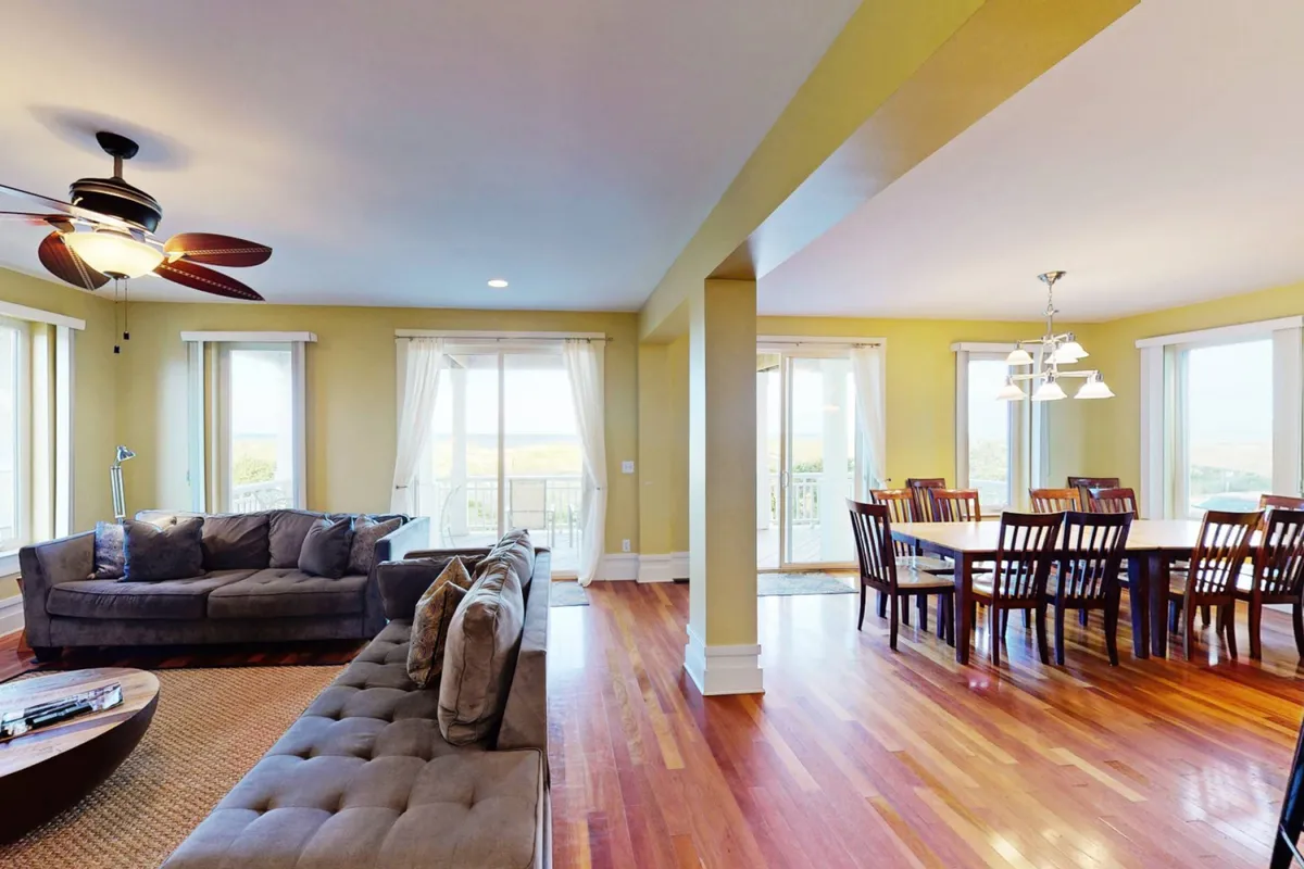 This image features a spacious, comfortable great room with a large sectional sofa and a sizable dining table placed near windows that frame scenic outdoor views. The room is bathed in natural light, emphasizing its welcoming and relaxed atmosphere—a perfect setting for movie nights, family gatherings, and casual conversations.